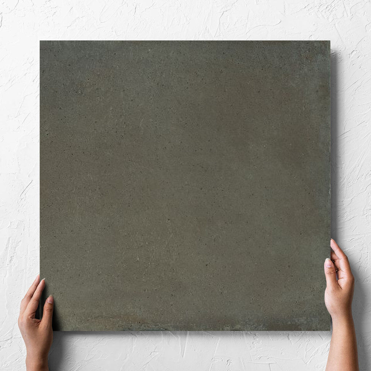 Hand holding a single Cotto Khaki Matt 600x600mm tile against a white rendered wall, showing the matt surface