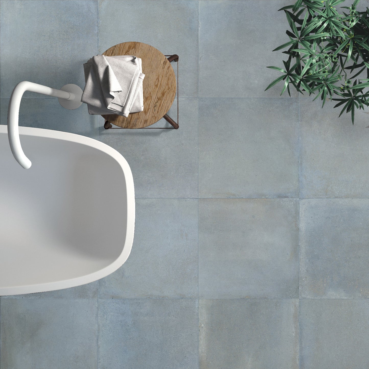 Overhead view of Cotto Sky Matt 600x600mm blue-grey concrete-effect floor tiles styled with a freestanding white bathtub, wooden side table, and indoor plant.