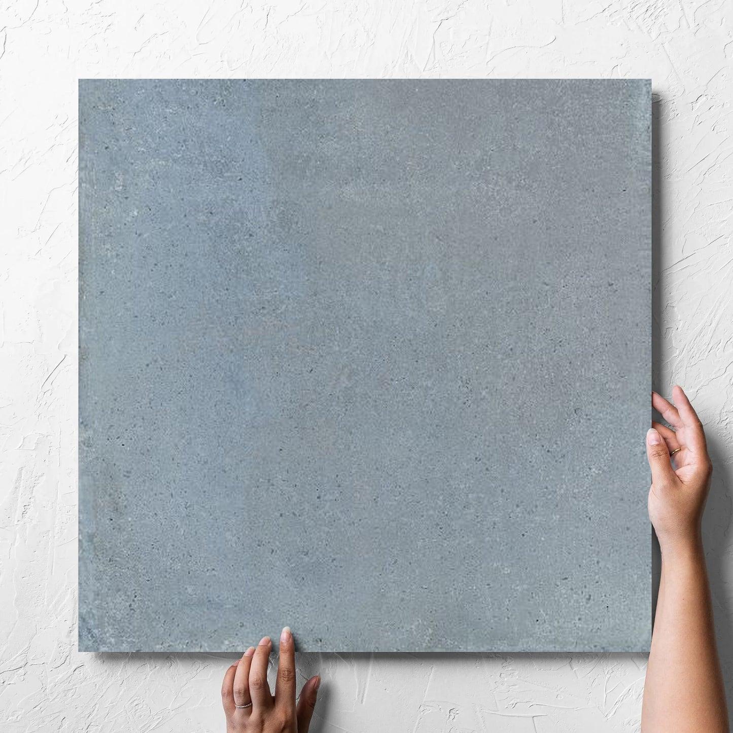 Hand holding a single Cotto Sky Matt 600x600mm tile against a white rendered wall, showing the matt surface