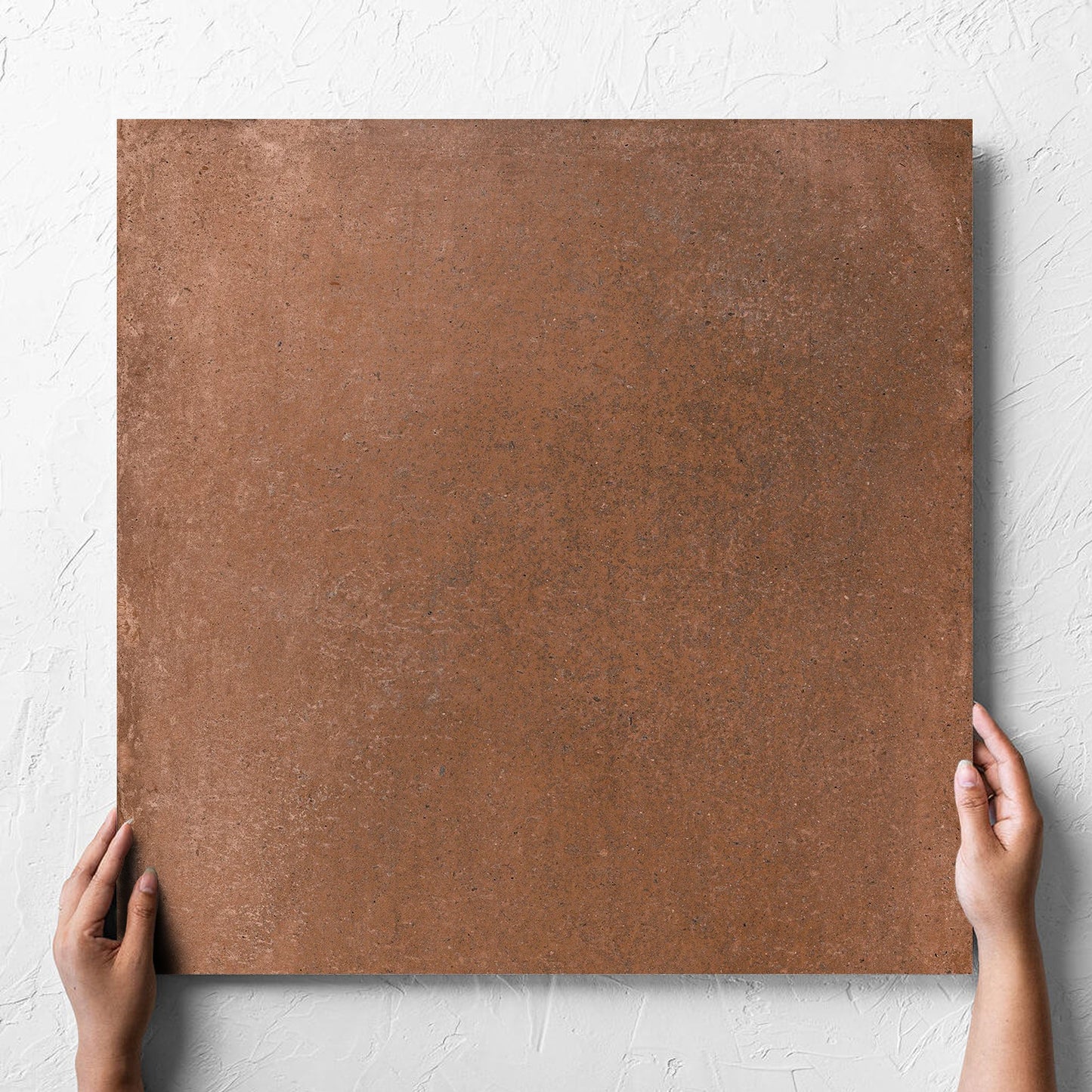 Hand holding a single Cotto Terra Matt 600x600mm tile against a white rendered wall, showing the matt surface