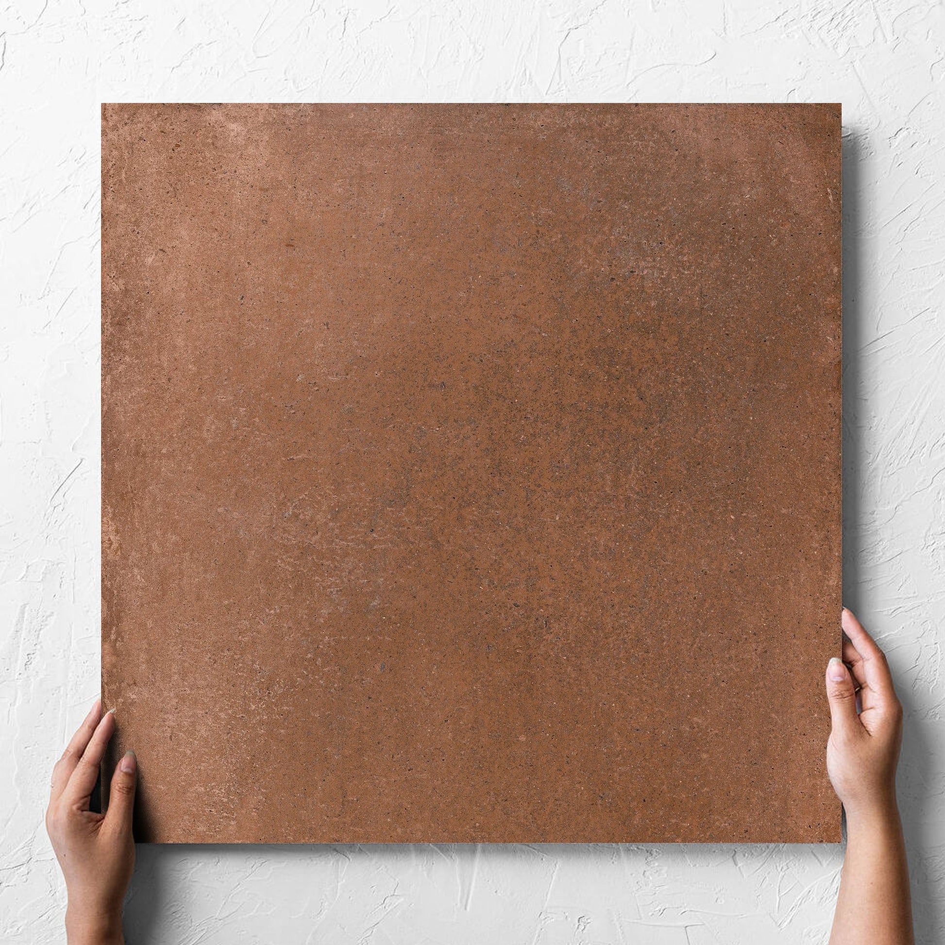 Hand holding a single Cotto Terra Matt 600x600mm tile against a white rendered wall, showing the matt surface