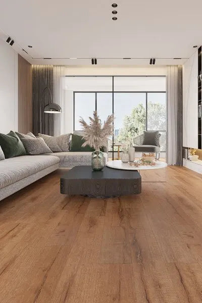 Country Oak Urban Laminate 12mm Flooring 12mm installed in a modern living room with a grey sectional sofa, dark wood coffee table, and large floor-to-ceiling windows.