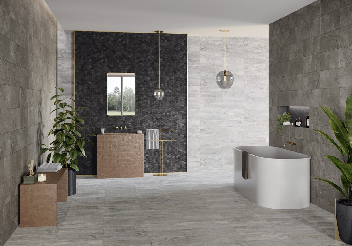 Courtyard Sterling Matt 300x600mm grey stone-effect tiles installed on bathroom walls and floor alongside a freestanding white bath, copper vanity, and hexagon mosaic feature wall with pendant lighting.