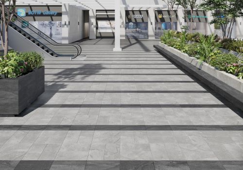 Courtyard Sterling Matt 300x600mm grey stone-look tiles installed across wide outdoor plaza steps with planters and retail shopfronts beyond.