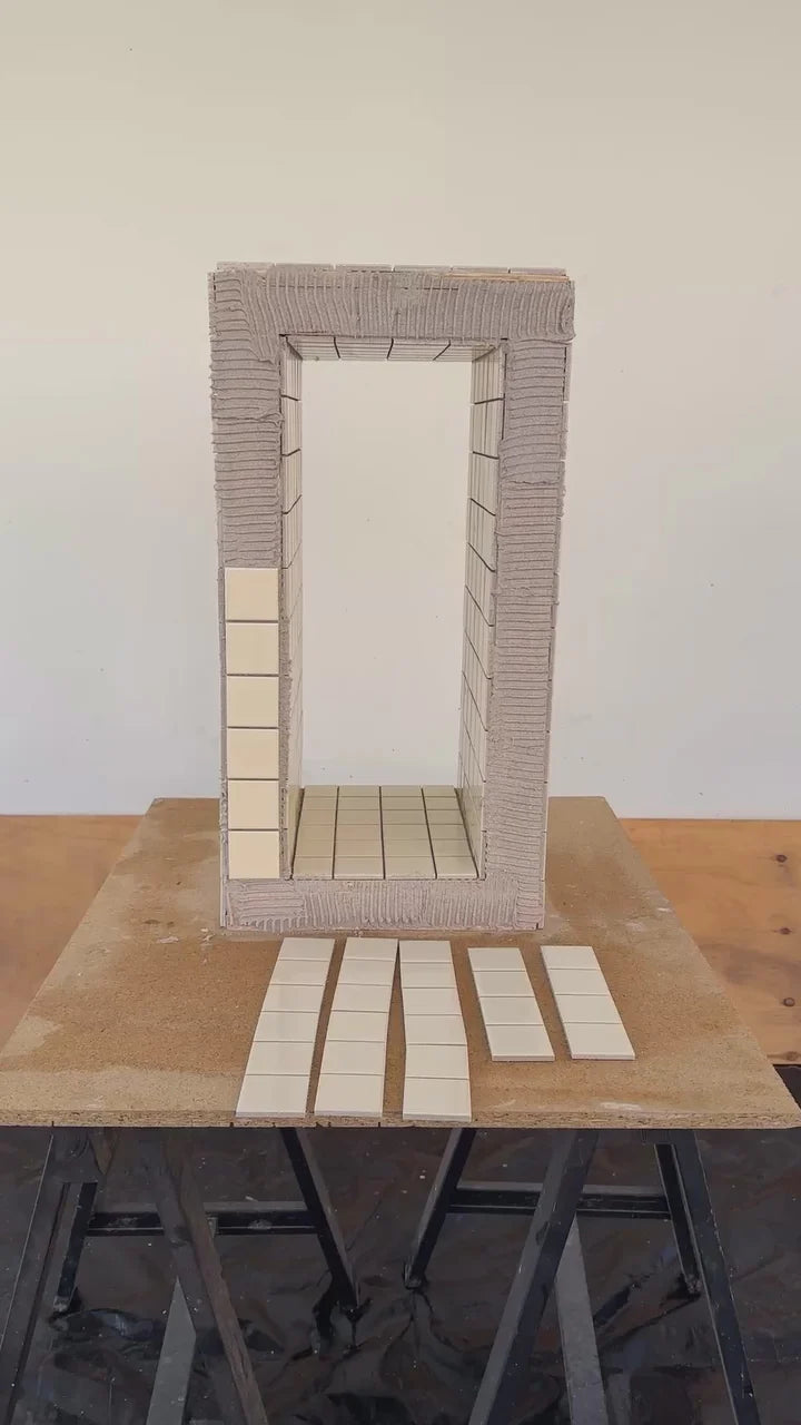Architectural scale model mockup showing Cream Gloss Porcelain Glazed 48x48mm Square tiles being dry-laid inside a miniature room frame with adhesive ridges visible on a timber workbench.