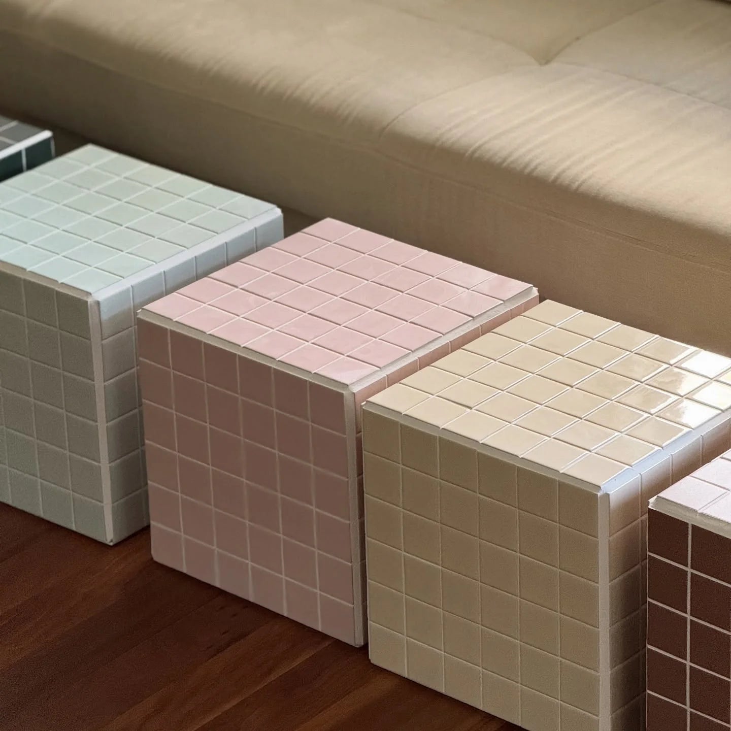 Cream Gloss Porcelain Glazed 48x48mm Square tiles covering decorative cubes displayed in a row alongside pink and mint coloured tile sample cubes on a timber floor.