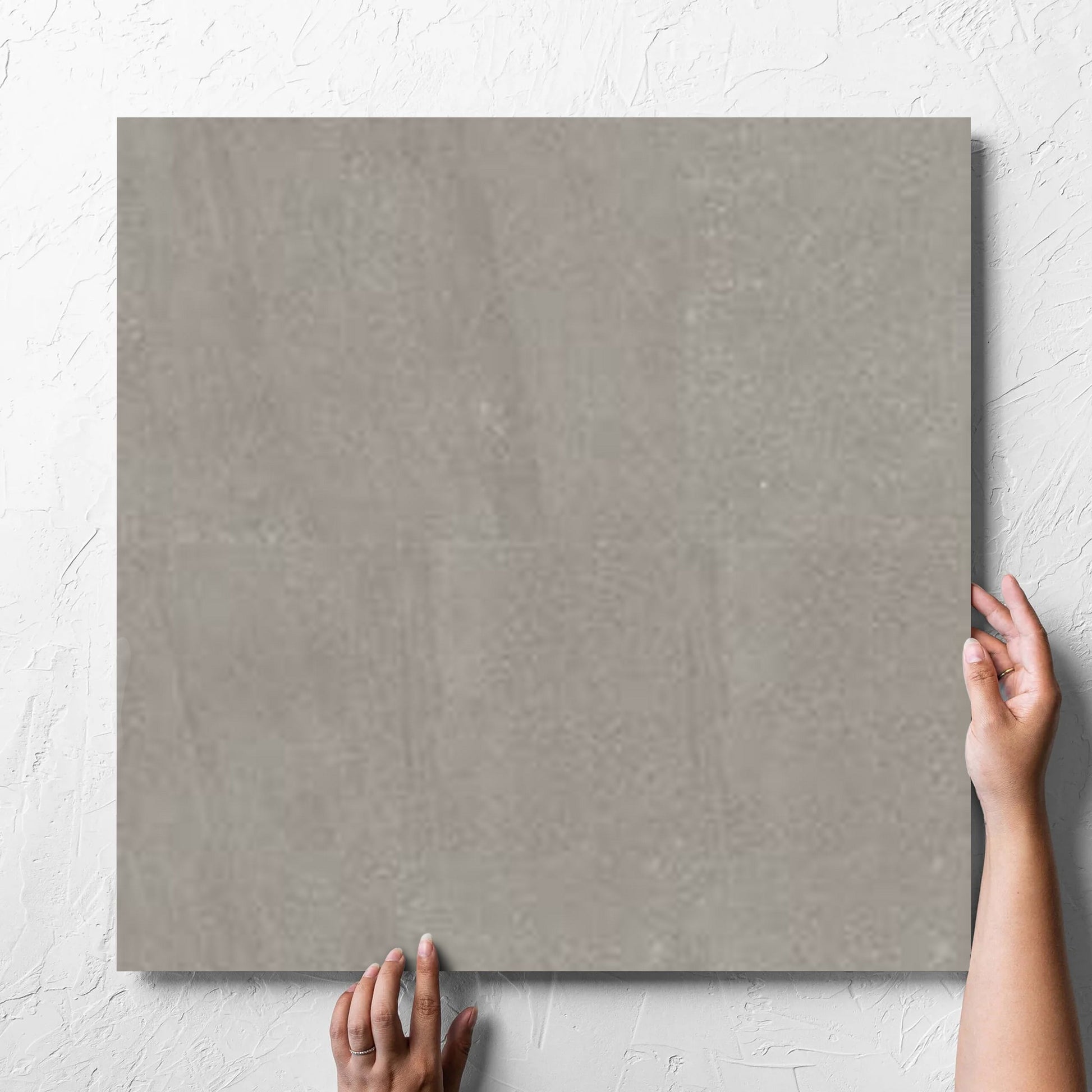 Hand holding a single Crystal Quartz Greige Matt Rectified 600x600mm tile against a white rendered wall, showing the tile surface
