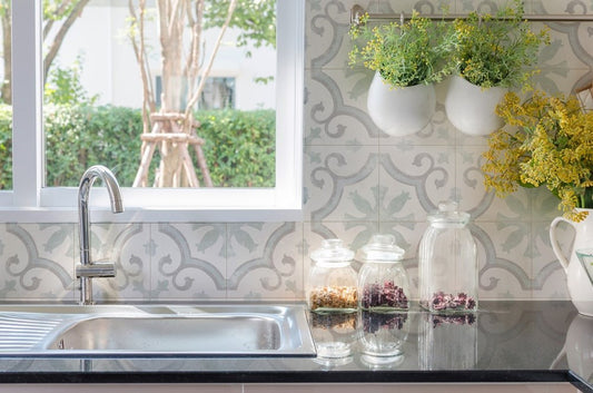Da Vinci Venetian Matt 200x200mm tiles used as a kitchen splashback with ornate grey pattern, styled with hanging herb pots, glass jars, and a stainless steel sink.