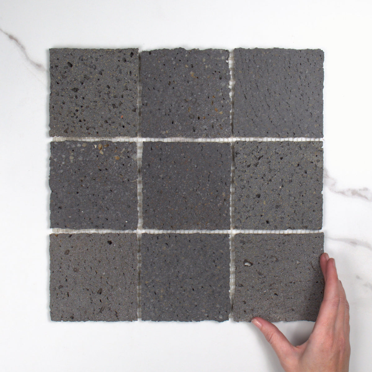 Elementa Travertine Black Mosaic 100x100mm top view, hand for scale