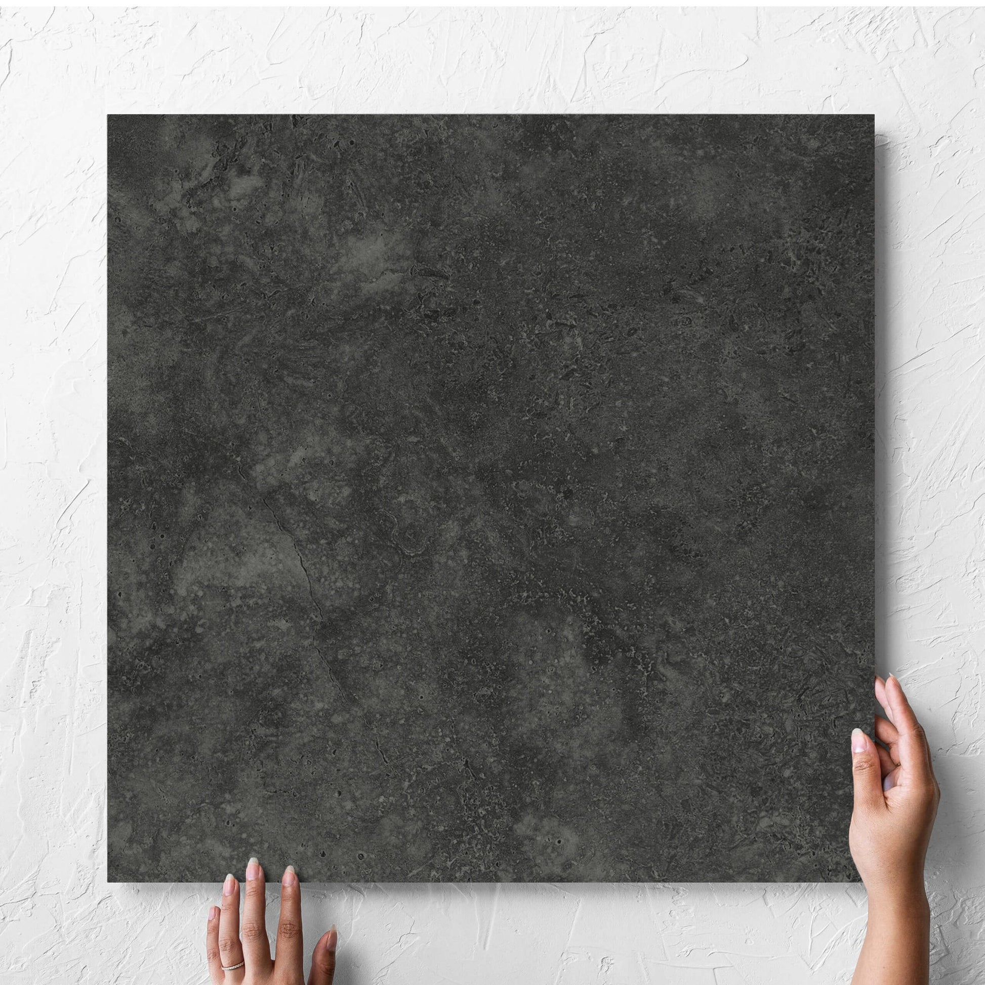 Hand holding a single Fossil Stone Coal Matt 600x600mm tile against a white rendered wall, showing the matt surface