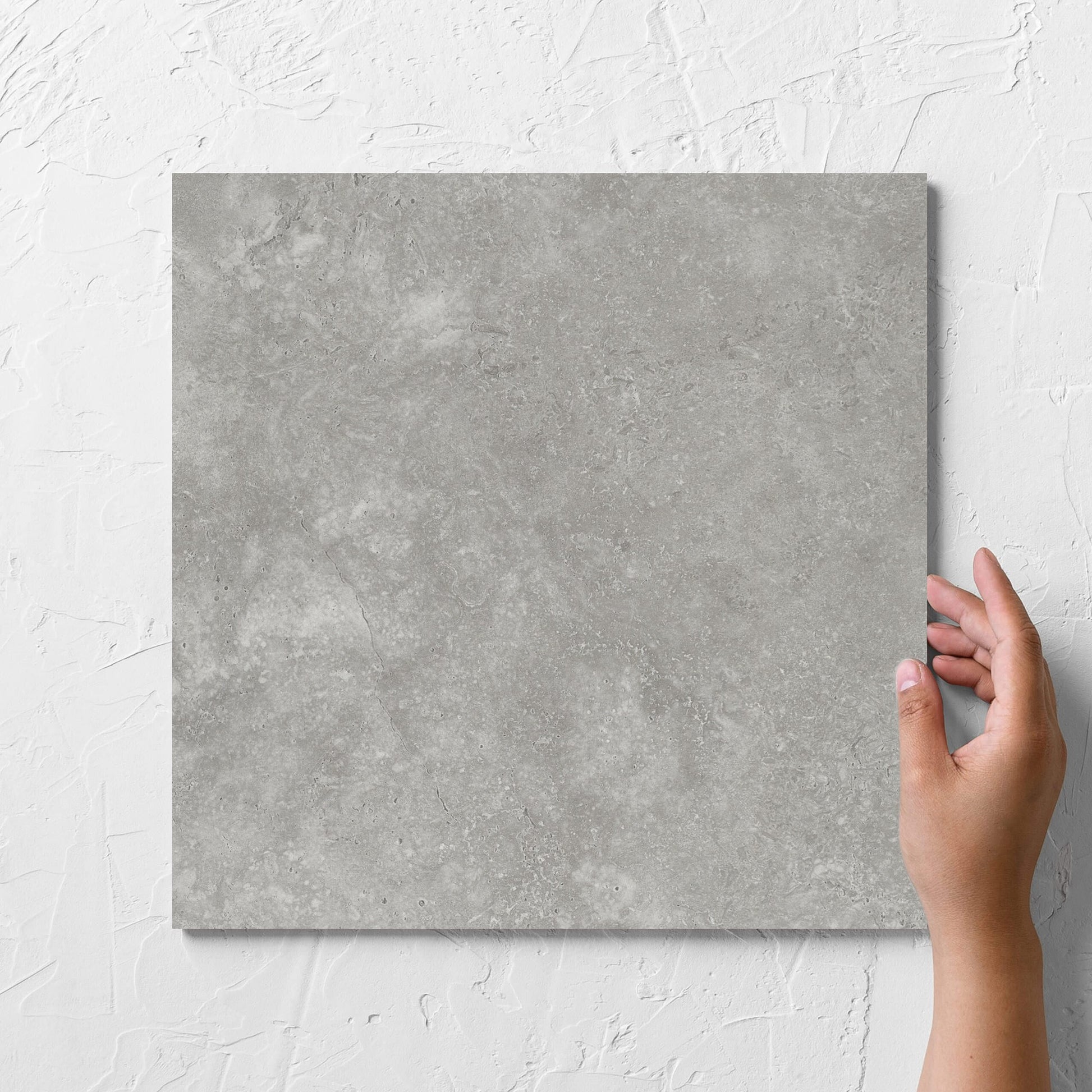 Hand holding a single Fossil Stone Pebble Matt 300x300mm tile against a white rendered wall, showing the matt surface