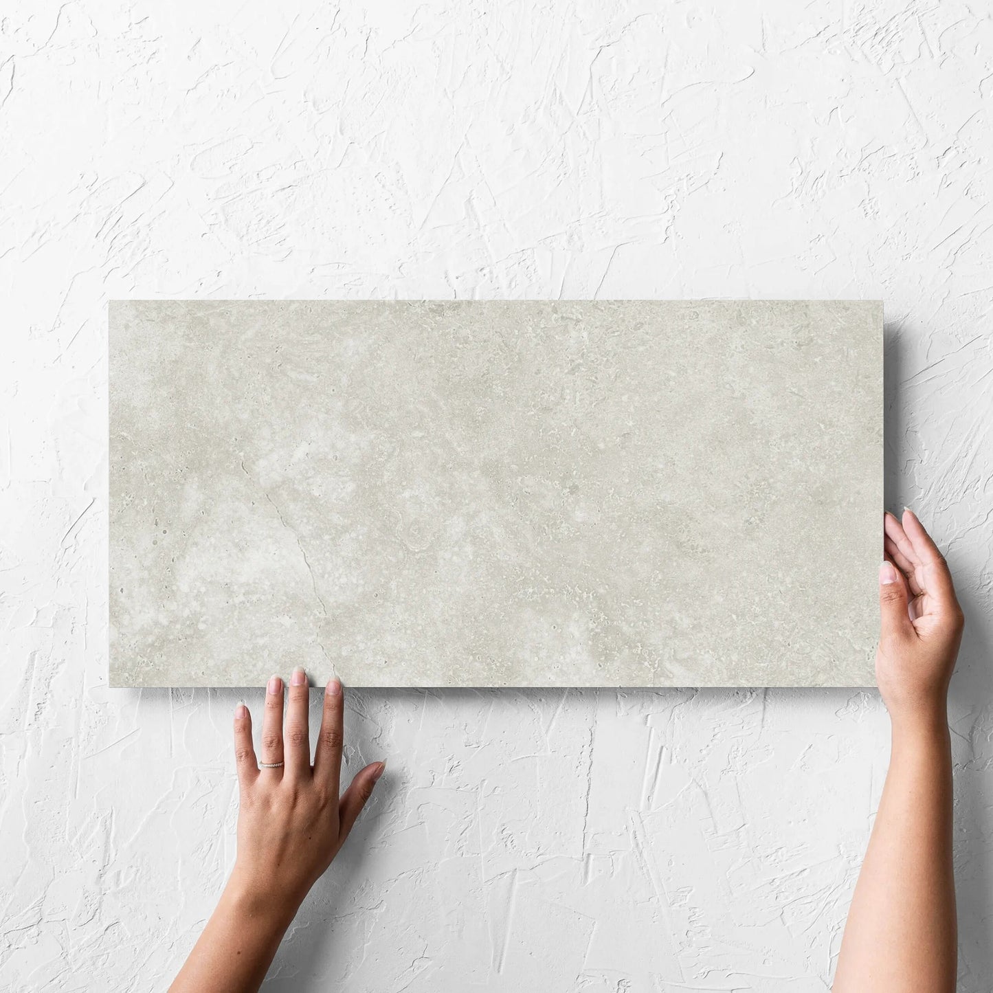 Hand holding a single Fossil Stone Sand Matt 300x600mm tile against a white rendered wall, showing the matt surface