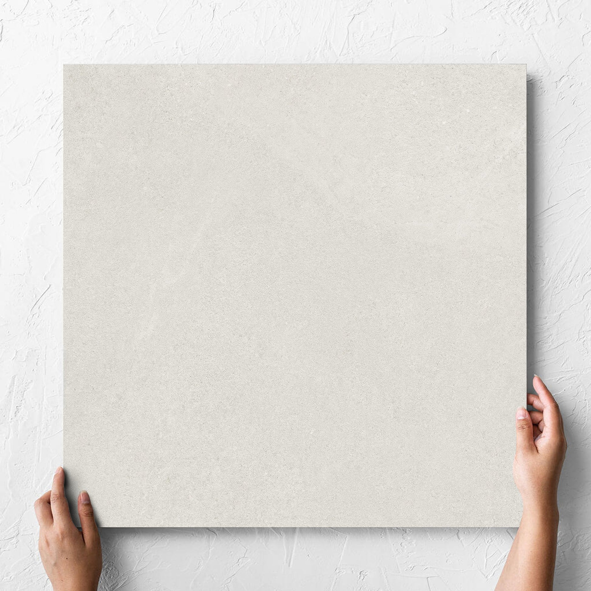 Hand holding a single Fusion Bianco Ultra Tech 600x600mm tile against a white rendered wall, showing the matt surface