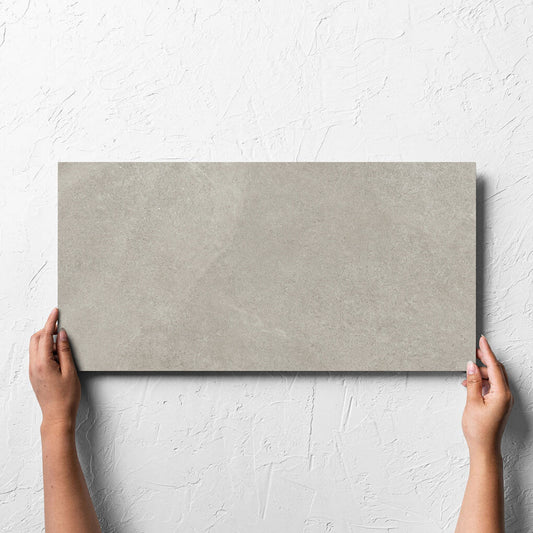 Hand holding a single Fusion Cenere Ultra Tech 300x600mm tile against a white rendered wall, showing the matt surface