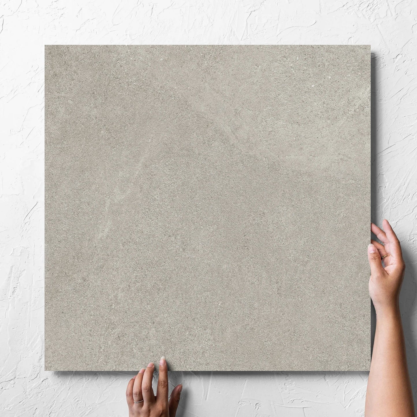 Hand holding a single Fusion Cenere Ultra Tech 600x600mm tile against a white rendered wall, showing the matt surface