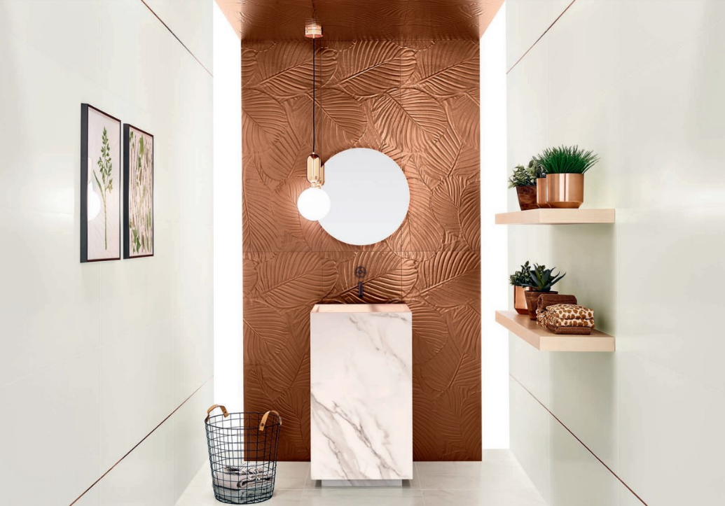 Genesis Leaf White 350x1000mm tiles installed as a copper-toned textured leaf-pattern feature wall in a luxury bathroom with marble pedestal vanity and pendant light.