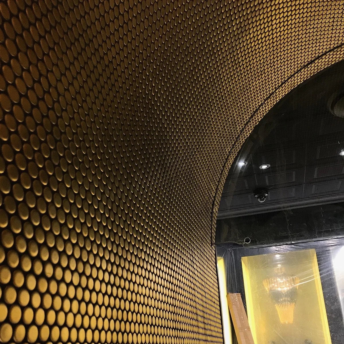 Gold Plated Matt Porcelain Glazed Penny Round 19mm tiles covering a curved arched entrance wall and ceiling, illuminated by recessed spotlights in a luxury interior.