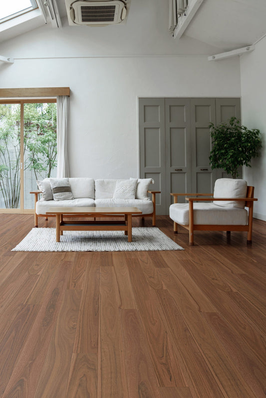 Grey Ironbark Engineered Australian Classic Flooring 14/3mm installed in a bright minimalist living room with timber-framed sofa, armchair, and sliding garden doors.