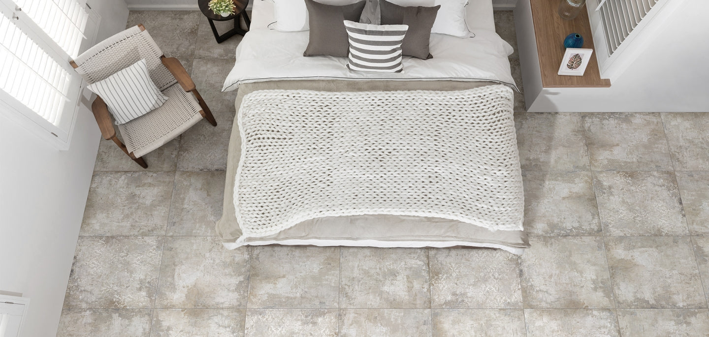 Grunge Beige Decor Rectified 600x600 floor tiles in a styled bedroom viewed from above, featuring a white knit throw and woven accent chair.