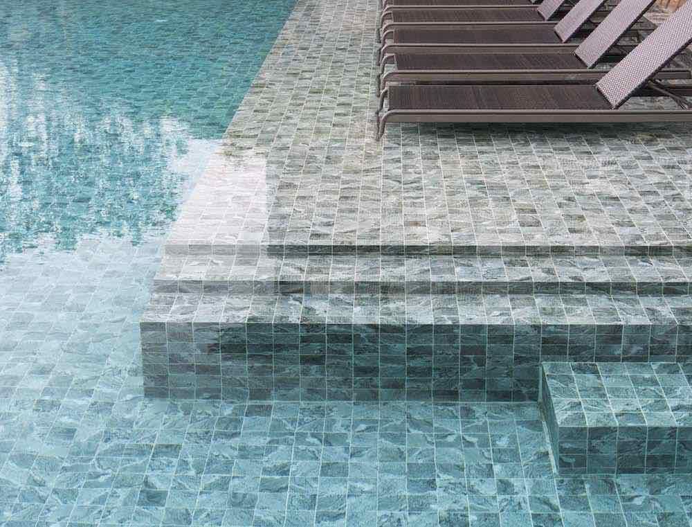 Hammond Green Mosaic 97x97mm tiles covering a luxury swimming pool's steps, coping edge, and surrounding deck with lounge chairs.