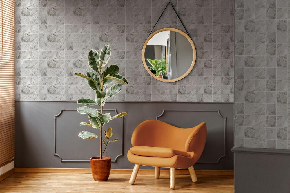Hammond Light Grey Mosaic 97x97mm tiles covering a feature wall in a stylish living room with an orange armchair, potted rubber plant, and round mirror.