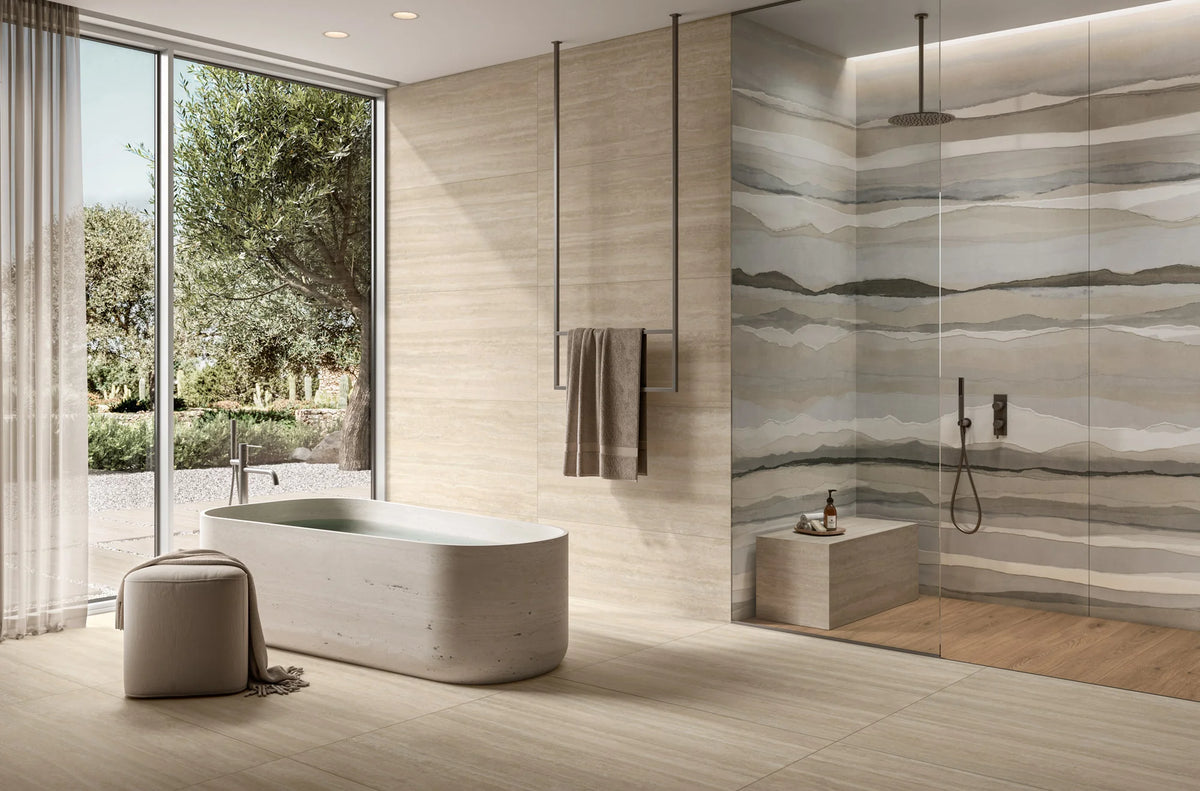 Ic.Verso Classico Gr 600x1200mm large-format beige stone-effect tiles installed across the floor and walls of a luxury spa bathroom featuring a freestanding travertine bath, walk-in shower with watercolour-effect feature wall, and floor-to-ceiling garden views.