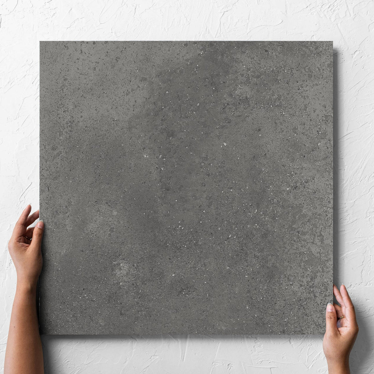 Hand holding a single Imperial Dark Grey Matt 600x600mm tile against a white rendered wall, showing the tile surface