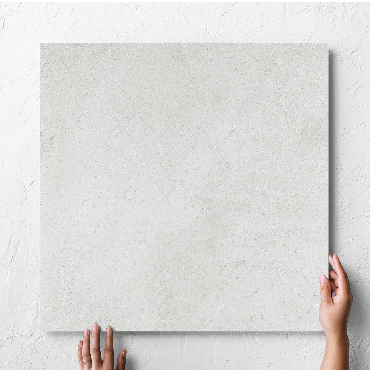 Hand holding a single Imperial Light Grey Matt 600x600mm tile against a white rendered wall, showing the tile surface