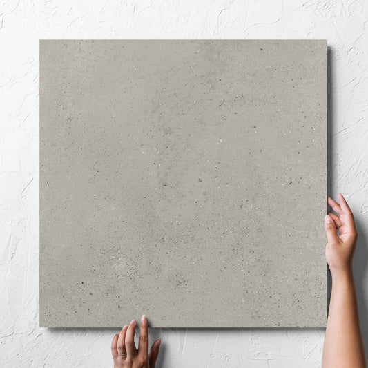 Hand holding a single Imperial Taupe Matt 600x600mm tile against a white rendered wall, showing the tile surface