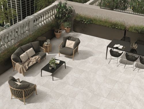 Isla Bone Matt 450x450mm tiles laid on a rooftop terrace patio featuring rattan outdoor furniture, lush potted plants, and a balustrade balcony.