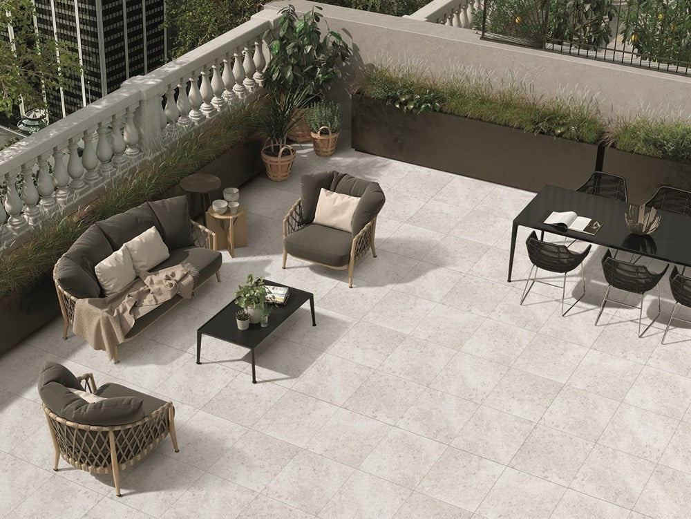 Isla Cloud Matt 450x450mm light grey stone-effect tiles laid on a rooftop terrace patio styled with wicker outdoor sofas and potted plants.