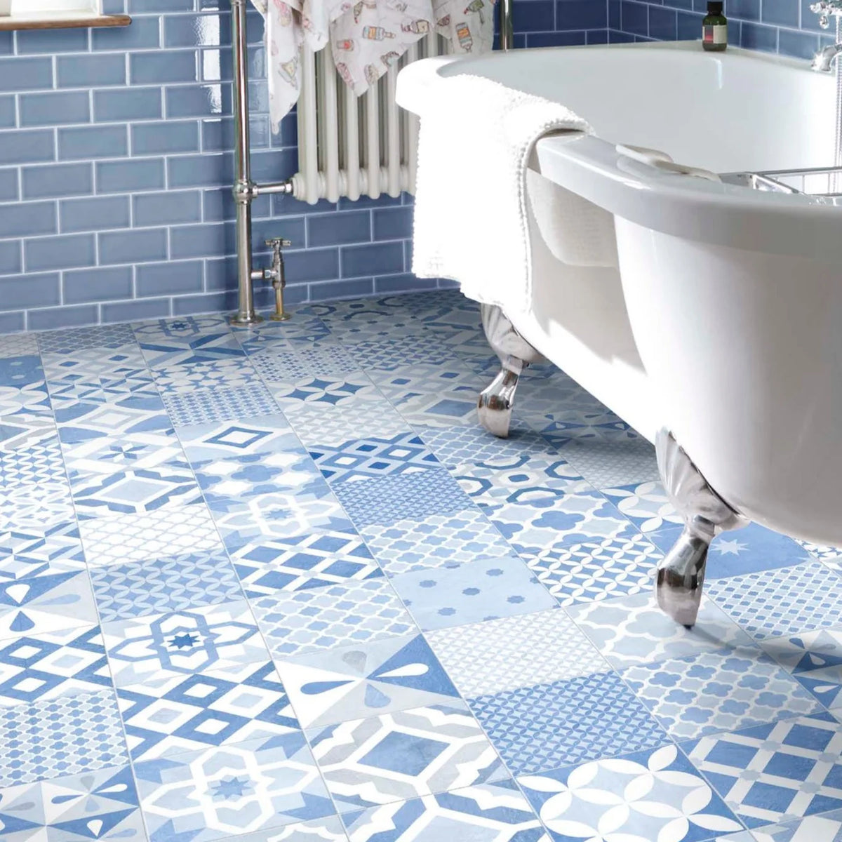 Island Minorca 205x205mm patchwork blue and white geometric tiles covering a bathroom floor beside a freestanding clawfoot bath and blue metro wall tiles.
