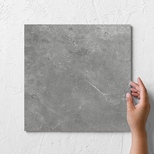 Hand holding a single Kashmir Ash Matt 300x300mm tile against a white rendered wall, showing the matt surface