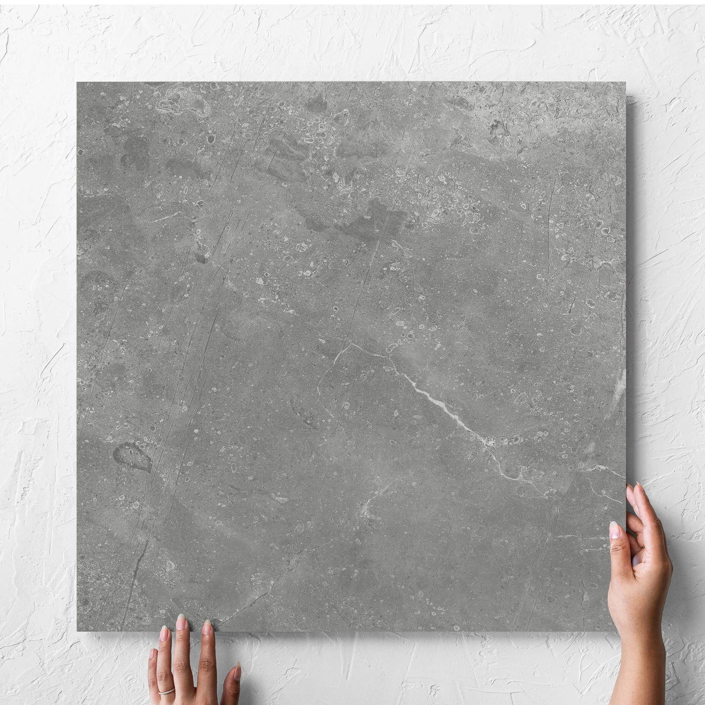 Hand holding a single Kashmir Ash Matt 600x600mm tile against a white rendered wall, showing the matt surface