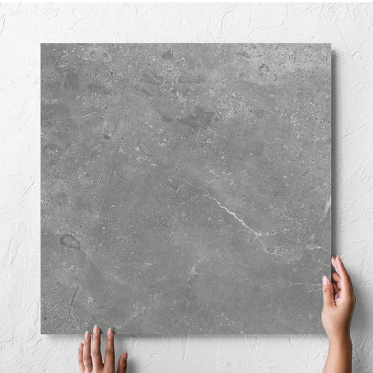 Hand holding a single Kashmir Ash Matt 600x600mm tile against a white rendered wall, showing the matt surface