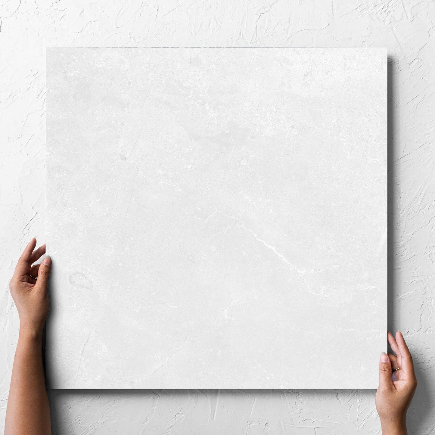 Hand holding a single Kashmir Bone Matt 600x600mm tile against a white rendered wall, showing the matt surface