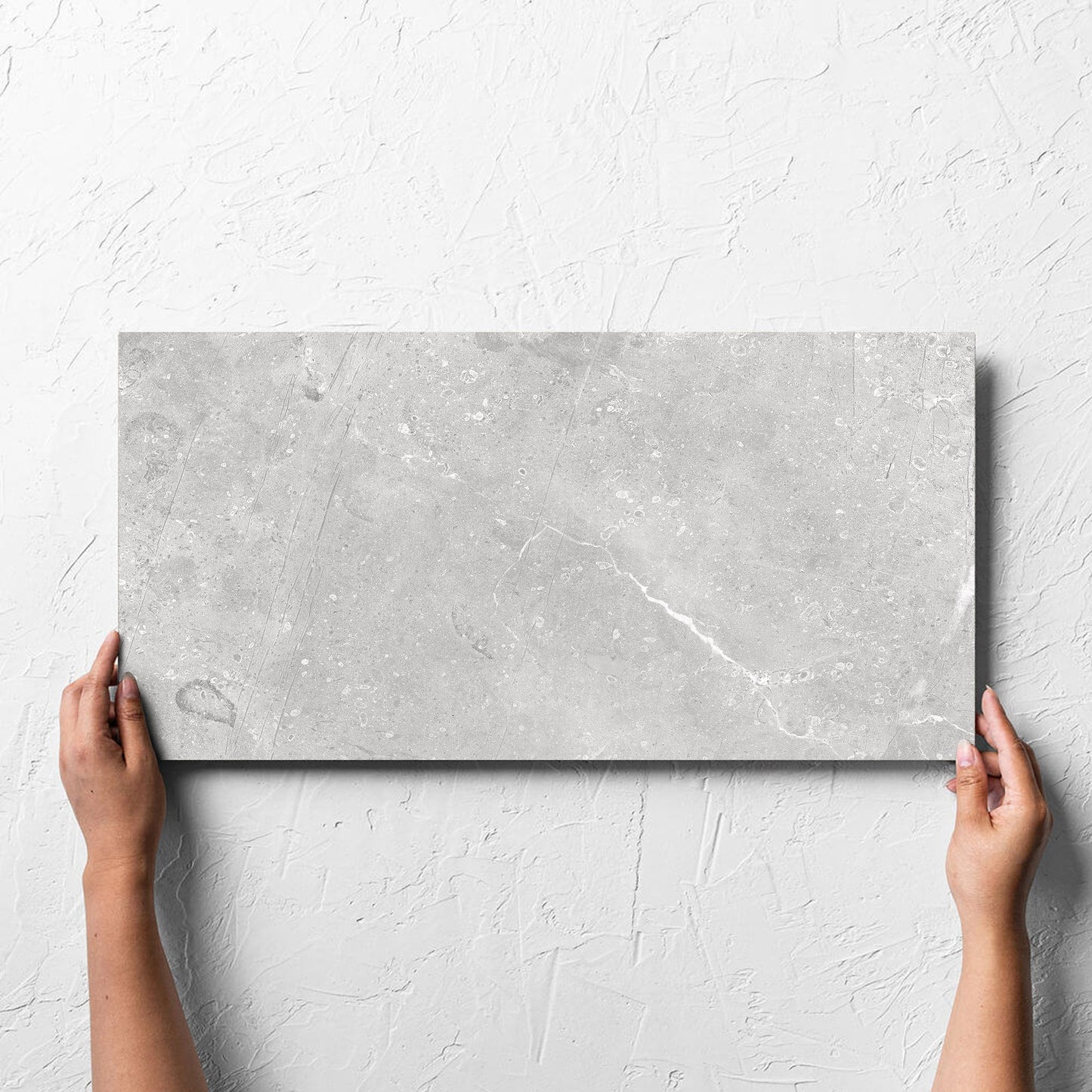 Hand holding a single Kashmir Stone Matt 300x600mm tile against a white rendered wall, showing the matt surface