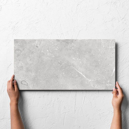 Hand holding a single Kashmir Stone Matt 300x600mm tile against a white rendered wall, showing the matt surface