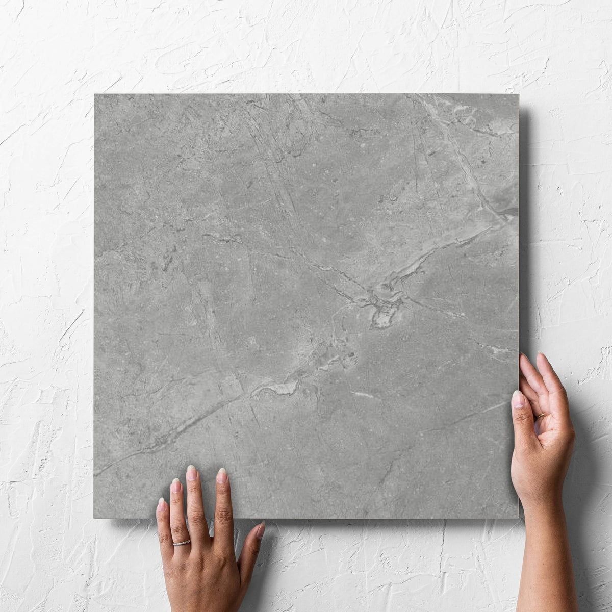 Hand holding a single Kashmir Stone Matt 450x450mm tile against a white rendered wall, showing the grey matt surface