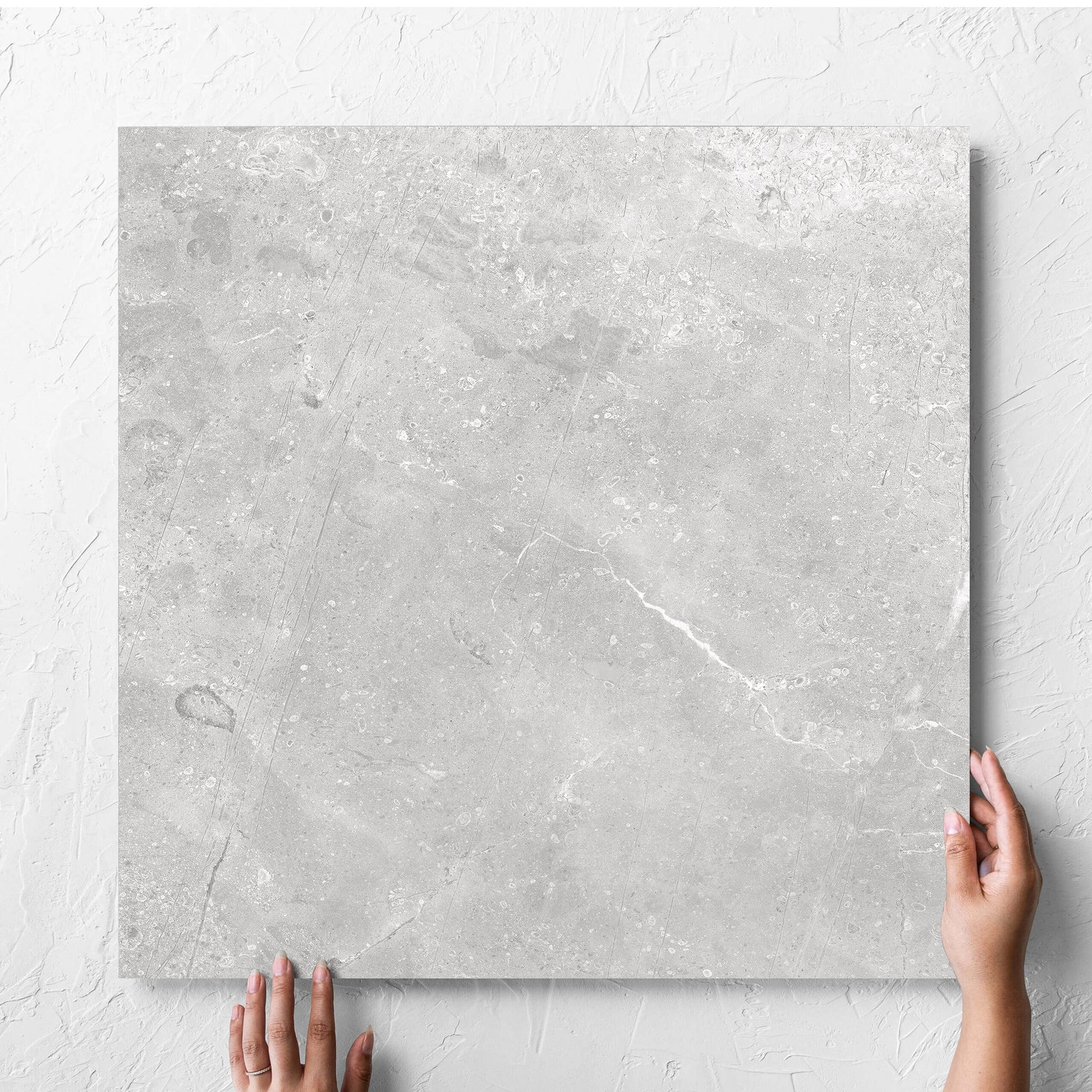 Hand holding a single Kashmir Stone Matt 600x600mm tile against a white rendered wall, showing the matt surface