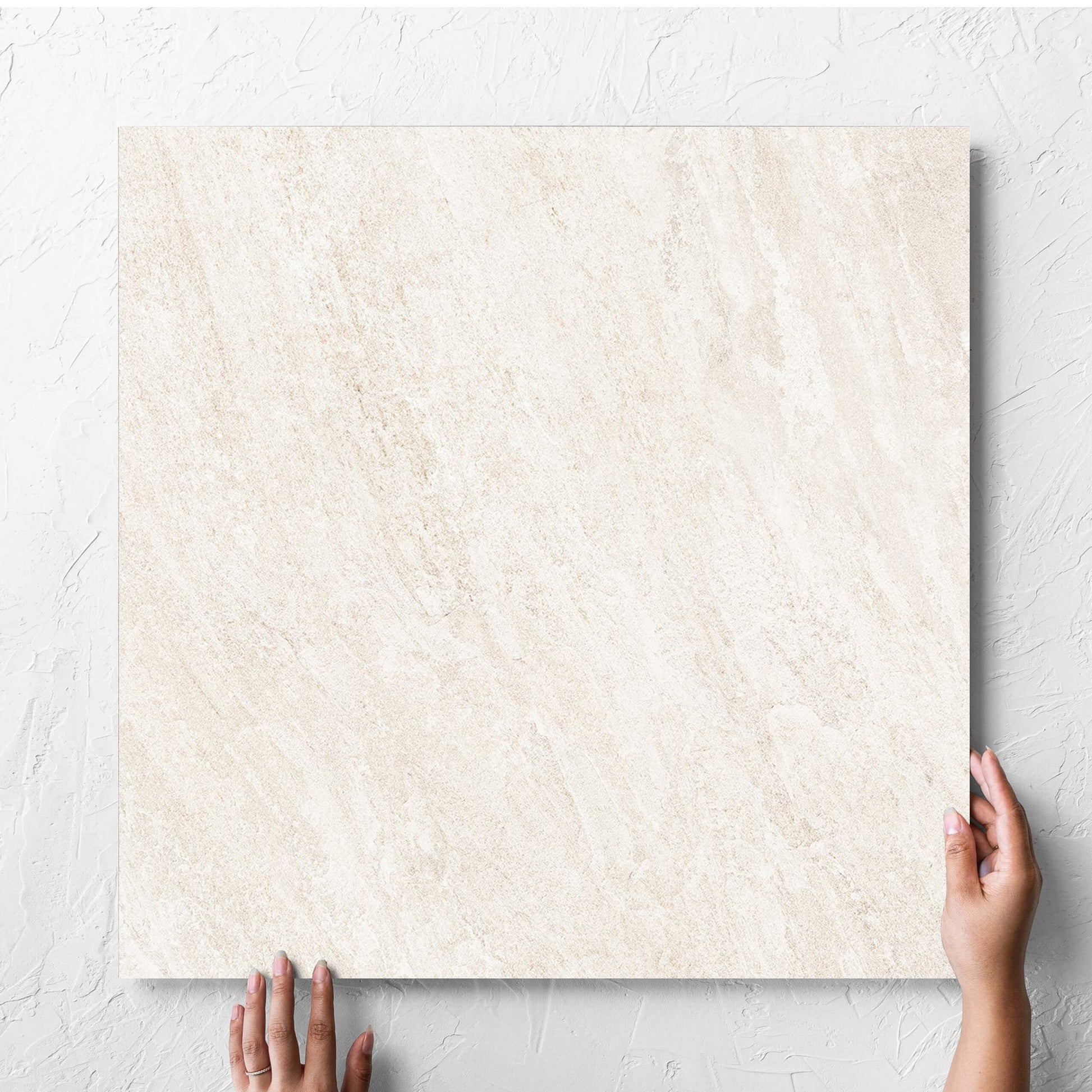 Hand holding a single Kora Stone Chalk Grip 600x600mm tile against a white rendered wall, showing the matt surface