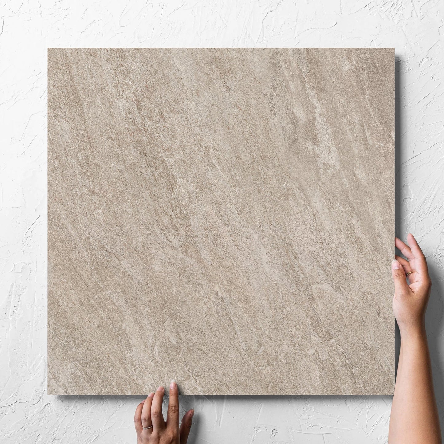 Hand holding a single Kora Stone Clay Matt 600x600mm tile against a white rendered wall, showing the matt surface