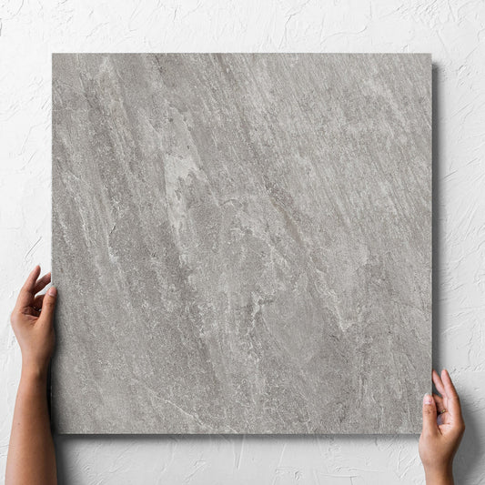 Hand holding a single Kora Stone Shale Matt 600x600mm tile against a white rendered wall, showing the matt surface
