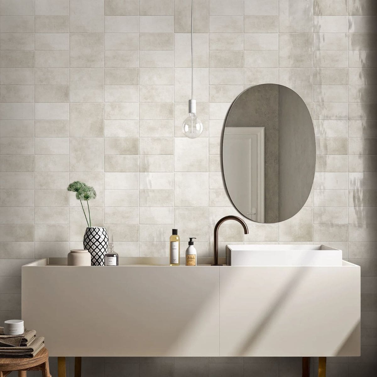 Krema Bloc Vanilla Gloss Krema Bloc Vanilla Gloss 125x125 tiles covering a full bathroom wall behind a minimalist white vanity unit, oval mirror, and pendant light.