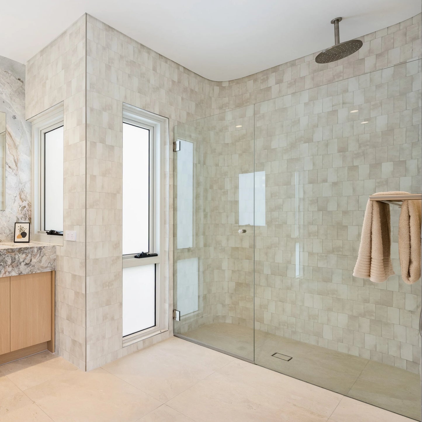 Krema Bloc Vanilla Gloss 125x125 tiles covering the walls of a spacious walk-in shower with frameless glass door, ceiling-mounted rain head, and timber vanity.