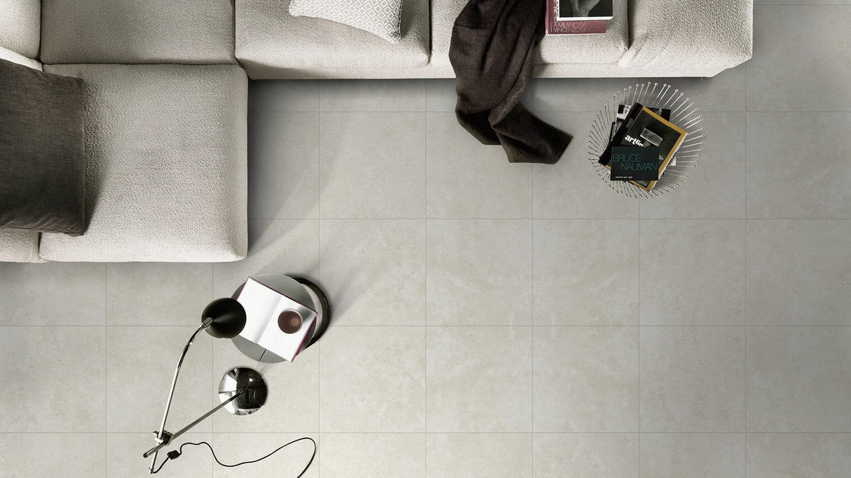 Kross Mid Grey Matt Smooth Grip 600x600mm floor tiles installed in a modern living room with a light grey sofa and floor lamp.