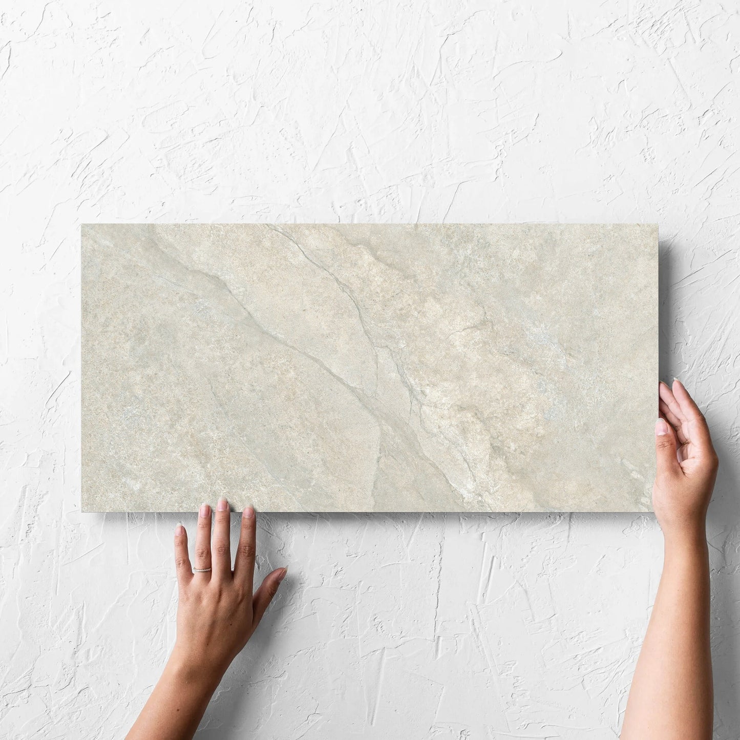 Hand holding a single Lakestone Grey Matt 300x600mm tile against a white rendered wall, showing the matt surface