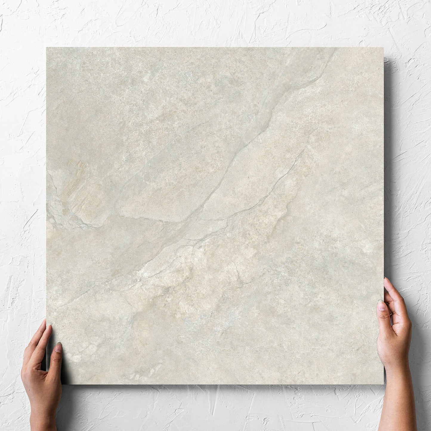 Hand holding a single Lakestone Grey Matt 600x600mm tile against a white rendered wall, showing the matt surface