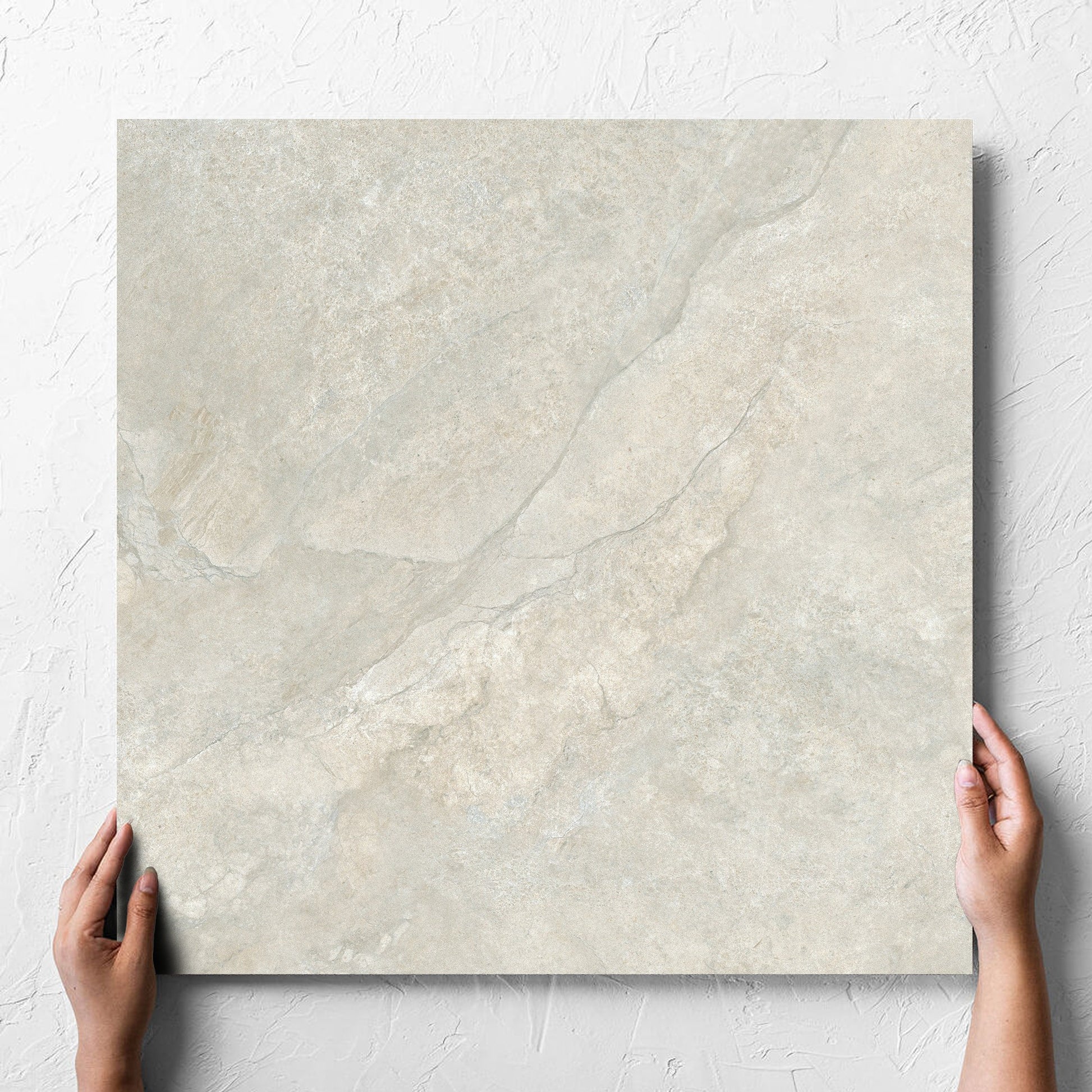 Hand holding a single Lakestone Grey Matt 600x600mm tile against a white rendered wall, showing the matt surface