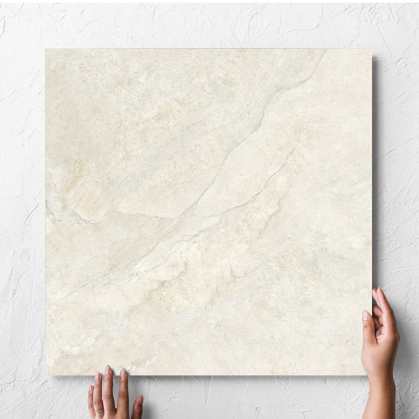 Hand holding a single Lakestone Sand Matt 600x600mm tile against a white rendered wall, showing the matt surface